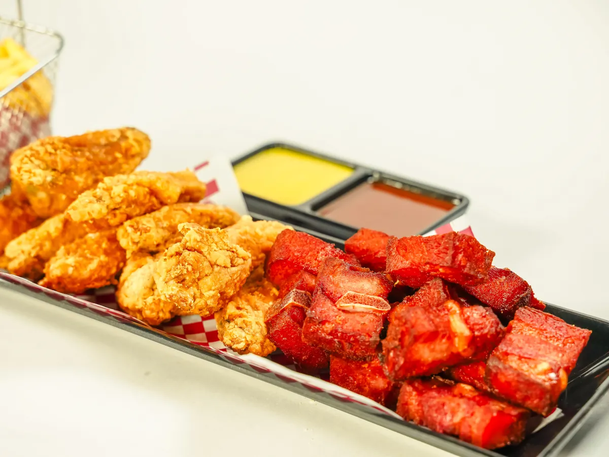 Bandeja con alitas apanadas y costillitas de cerdo servidas juntas, con salsas y papas a la francesa